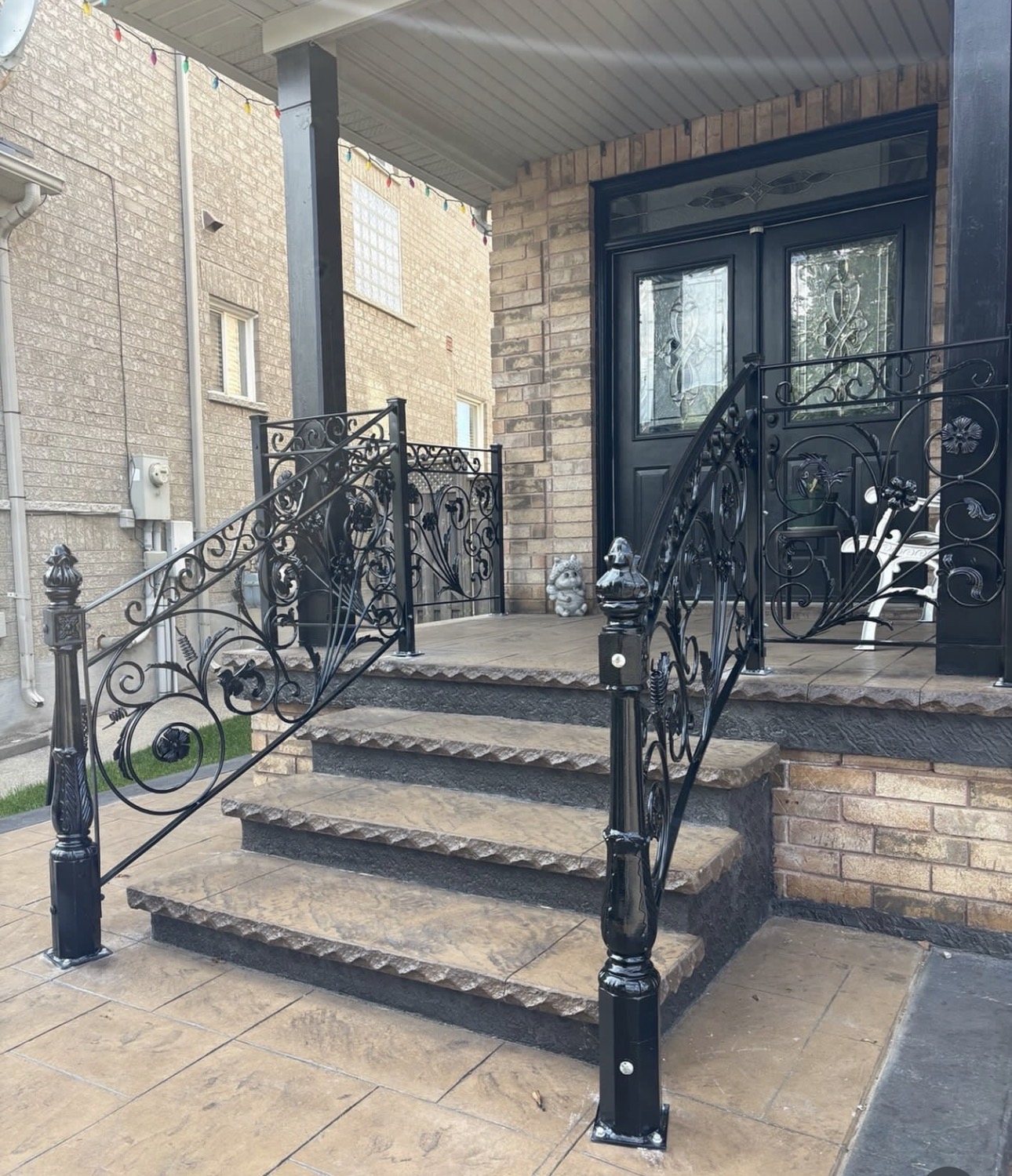 Black wrought iron porch stair railings and side panels with floral scrollwork on a brick home