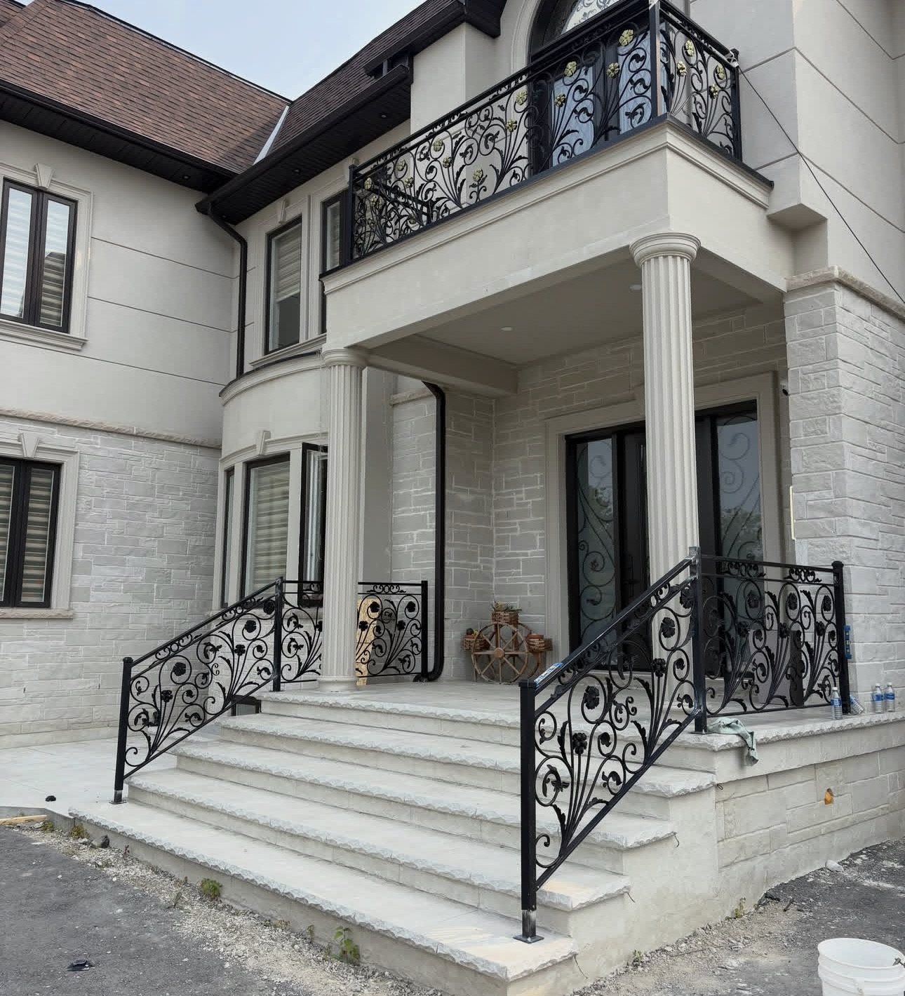 Black wrought iron balcony and entrance stair railings with floral scrollwork and gold accents on a stone-clad home